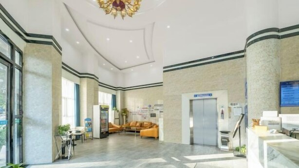 Een ruime lobby met een moderne kroonluchter, zithoek, receptiebalie en een zichtbare lift.