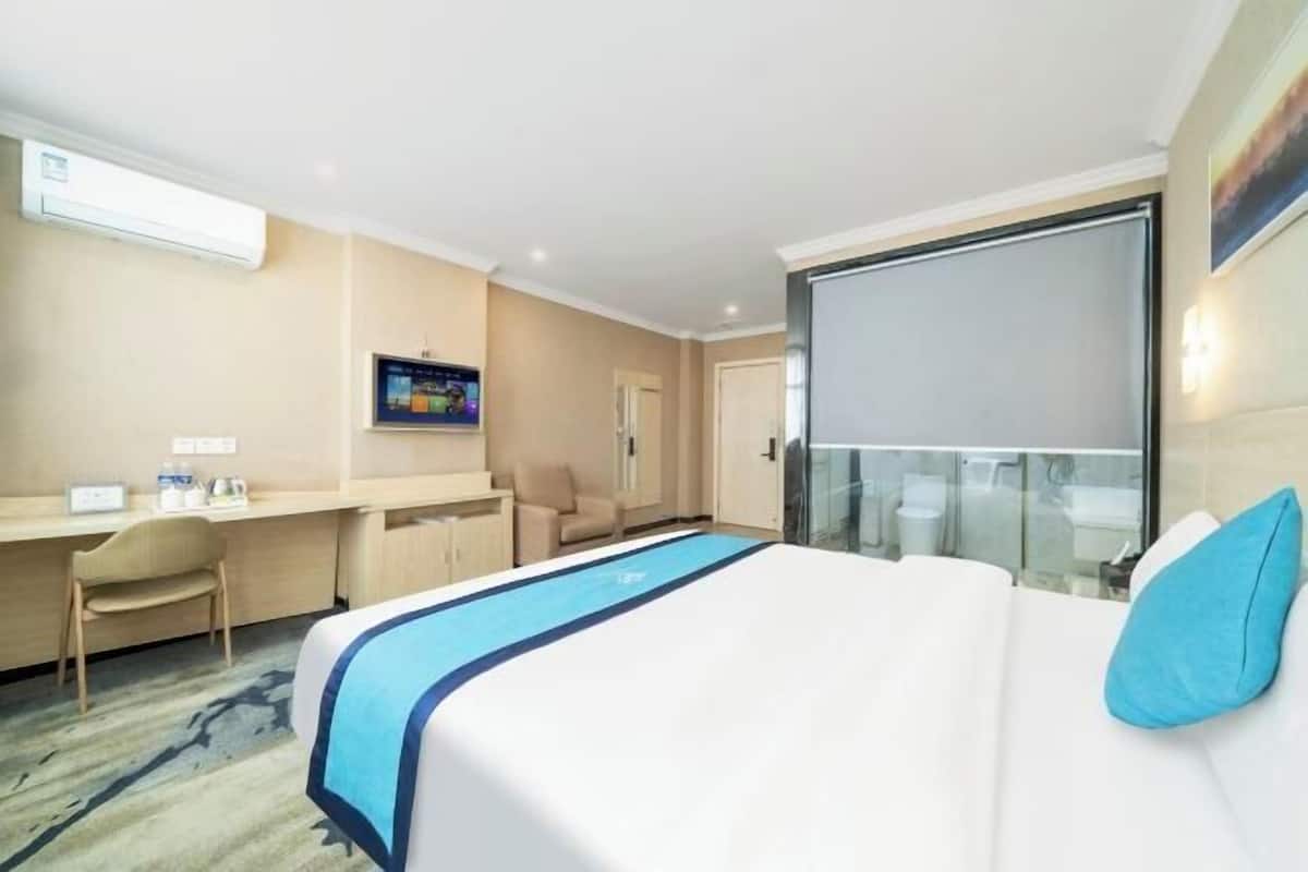 Ein Hotelzimmer mit einem Bett, einem Schreibtisch, einem Sessel, einem Fernseher und einer Schiebetür zum Balkon.