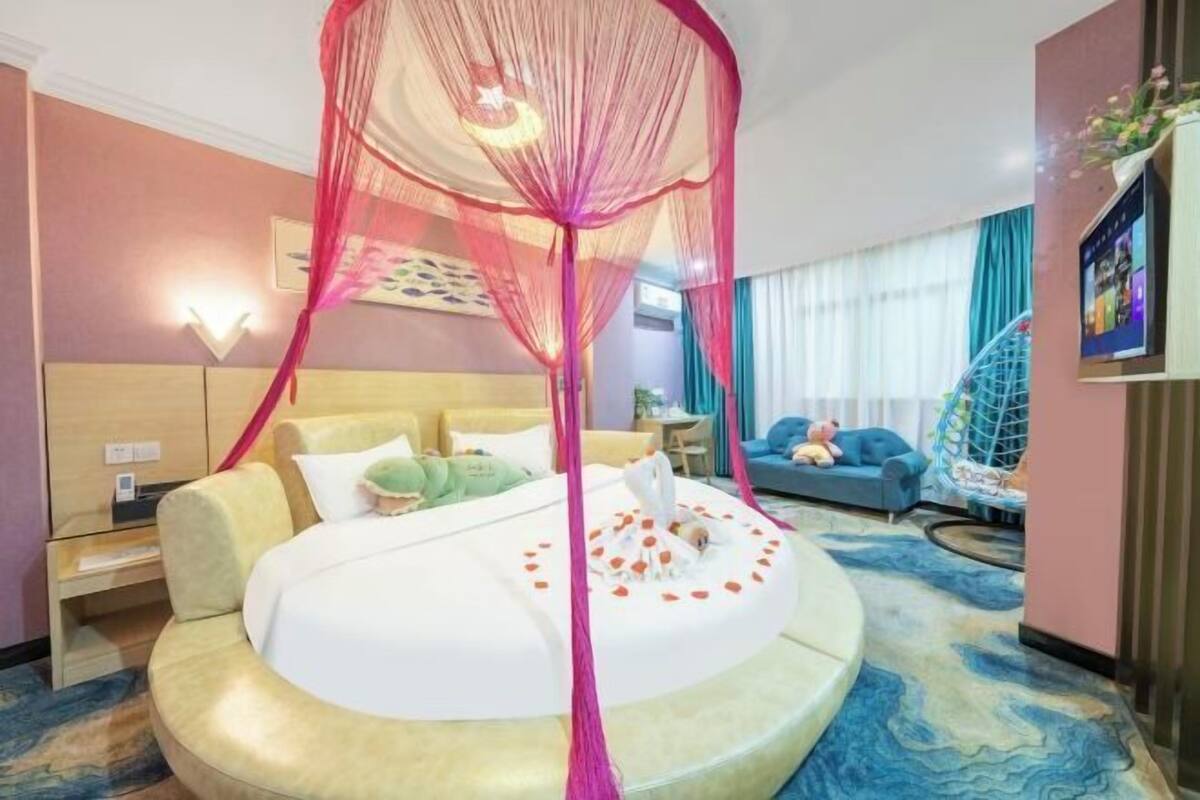 Ein Hotelzimmer mit einem Rundbett, einem Baldachin, einer Couch, einem Fernseher und einer Wendeltreppe.