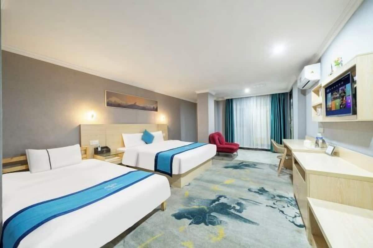 Ein Hotelzimmer mit zwei Betten, einem Schreibtisch, einem Stuhl, einem Fernseher und einem Bild an der Wand.