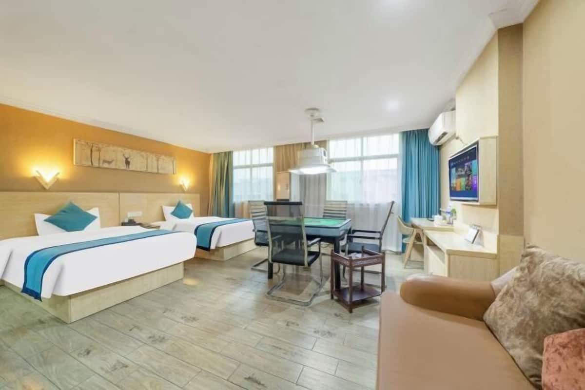 Ein Hotelzimmer mit zwei Betten, einem Schreibtisch, einem Sessel, einer Couch und einem Fernseher.
