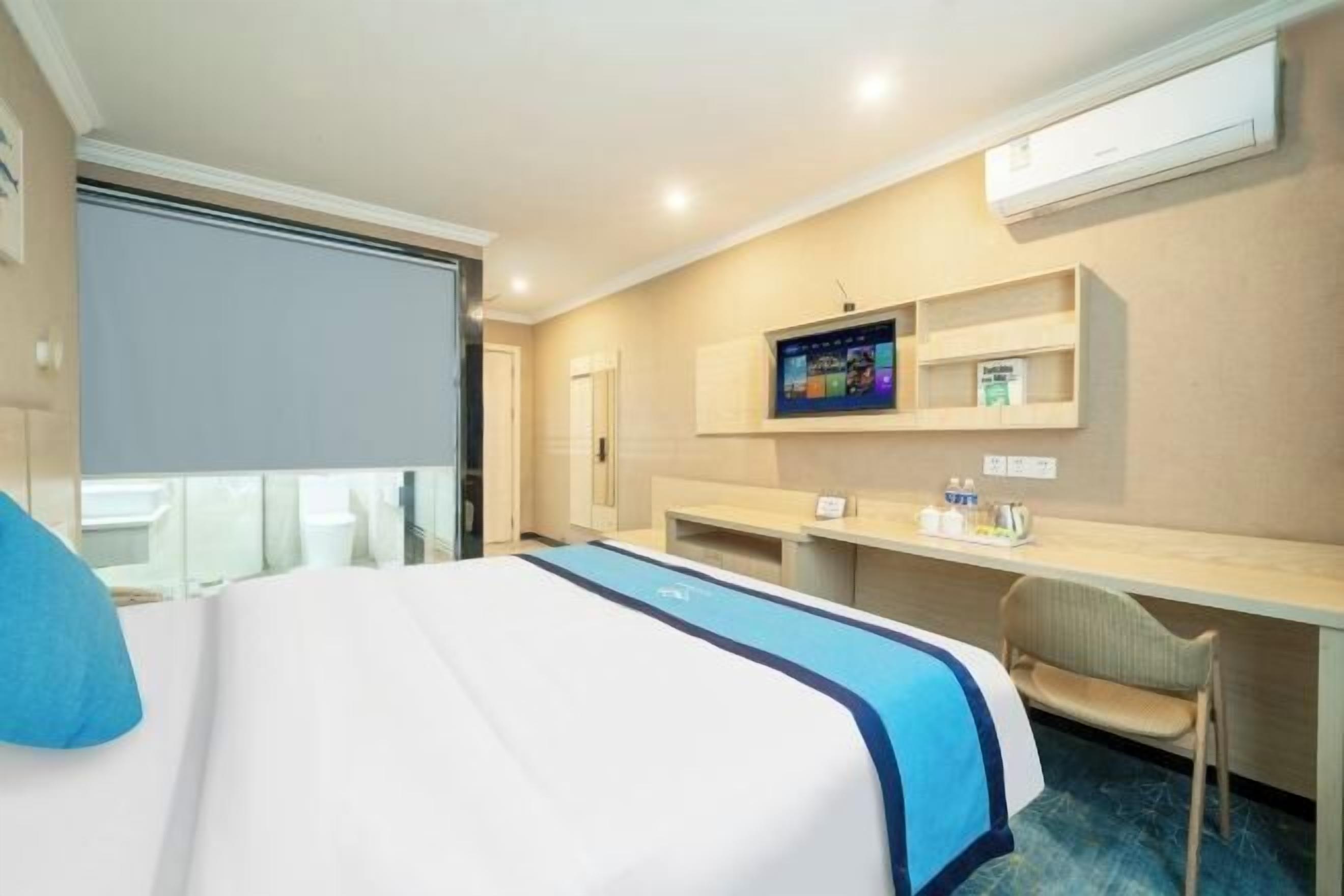 Ein Hotelzimmer mit Bett, Schreibtisch, Stuhl, Fernseher und Klimaanlage.