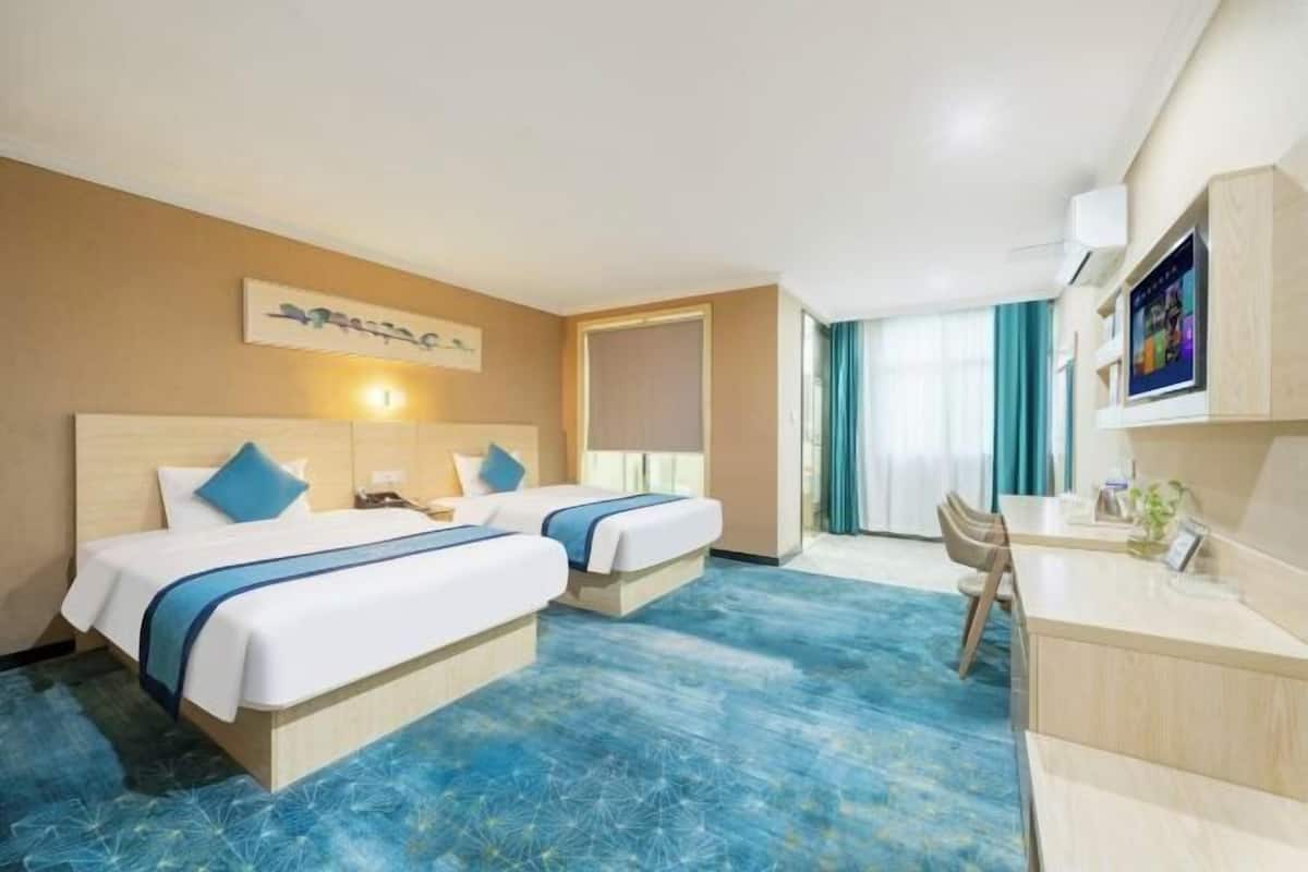 Ein Hotelzimmer mit zwei Betten, einem Schreibtisch, einem Stuhl, einem Fernseher und einem Fenster mit Vorhängen.
