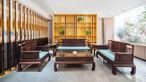 A lobby with wooden furniture, a glass coffee table, and a shelving unit with plants. - Kaimei Convenience Hotel (Nanning Jinxiang Avenue Subway Station) (Nanning)