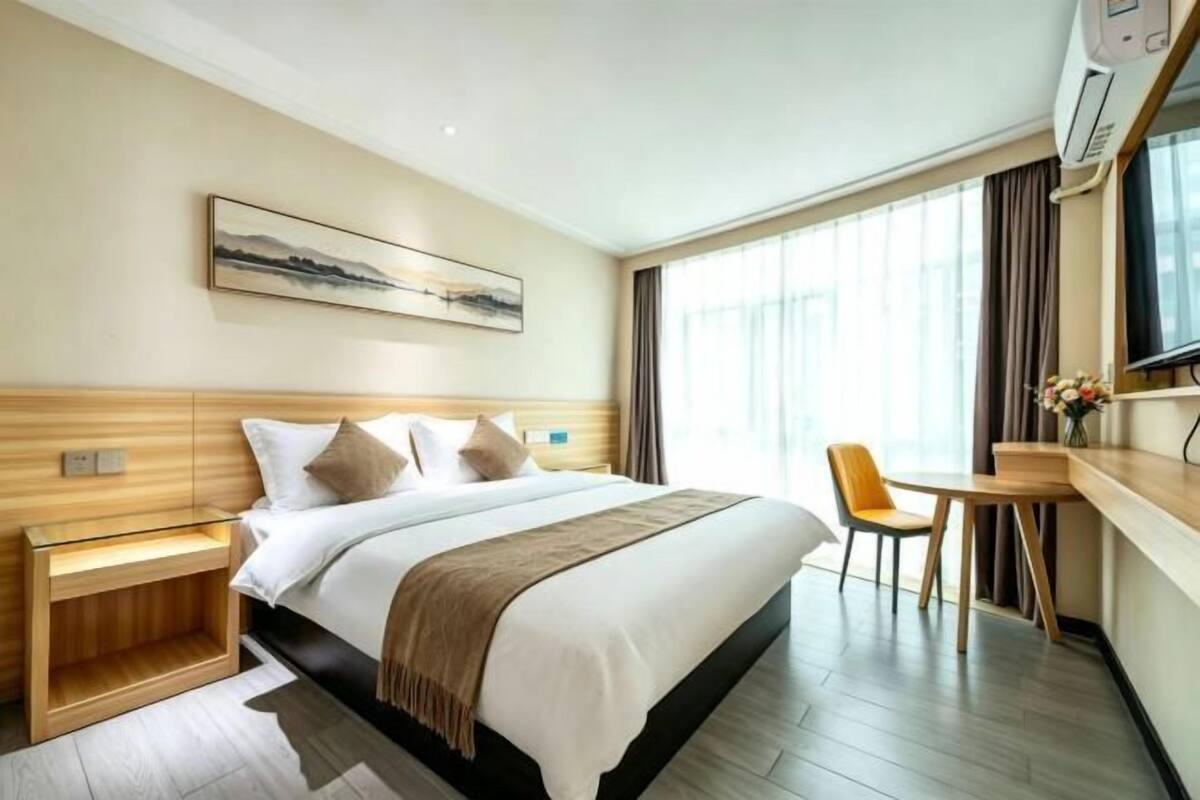 A hotel room with a bed, bedside table, chair, and a painting on the wall.