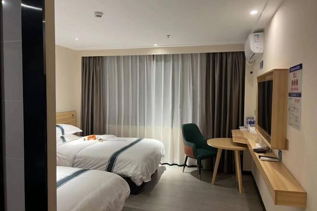 A hotel room with two beds, a desk, a chair, and a television.