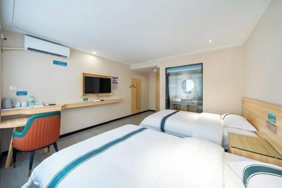 A hotel room with two beds, a desk, a chair, a TV, and a bathroom.