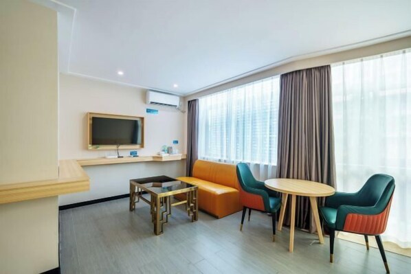 A hotel room with a sofa, a small table, a TV, and a window with curtains.