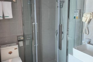 A modern bathroom with a glass shower enclosure, a toilet, and a hand dryer.