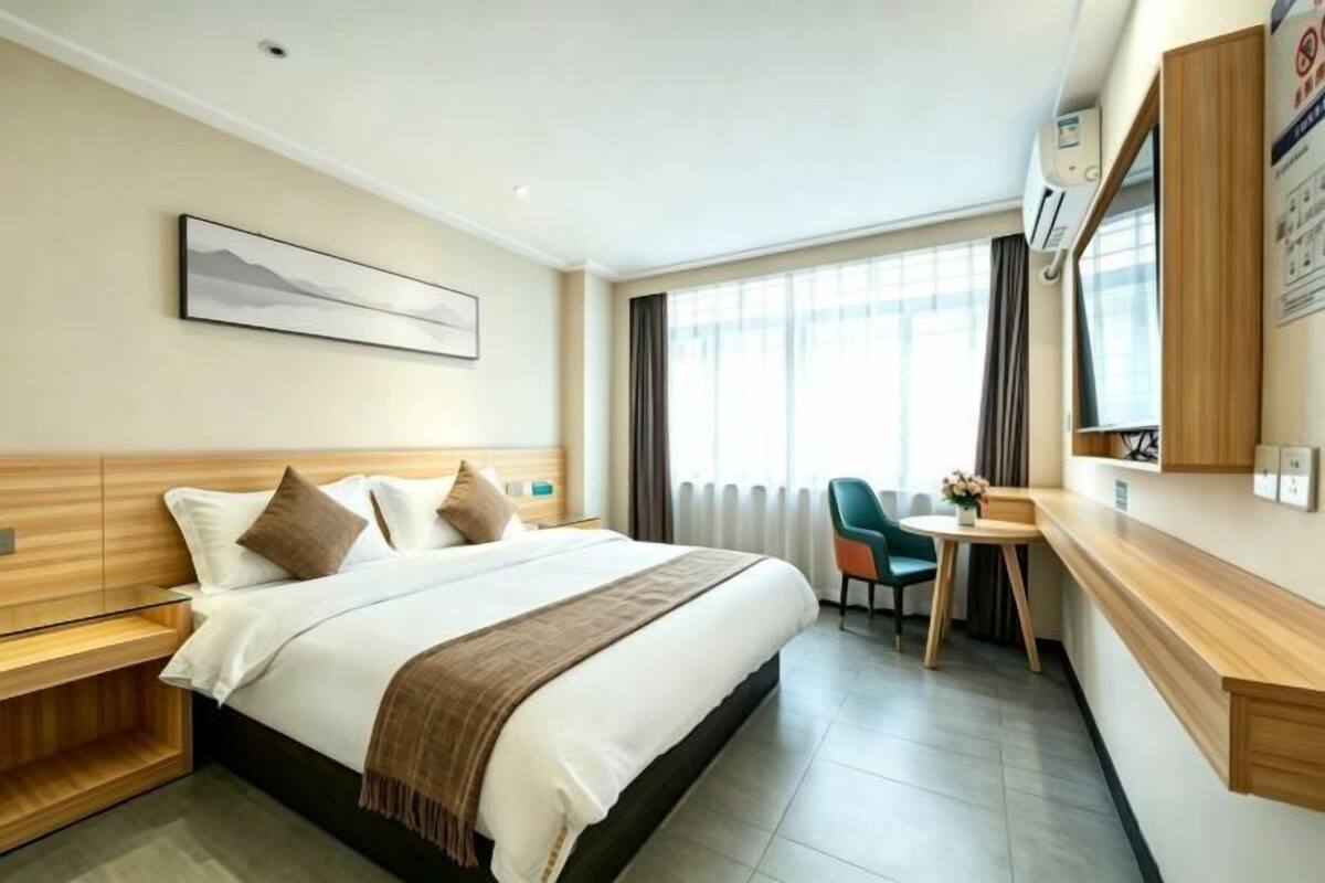 A hotel room with a bed, bedside table, desk, chair, and a window with curtains.