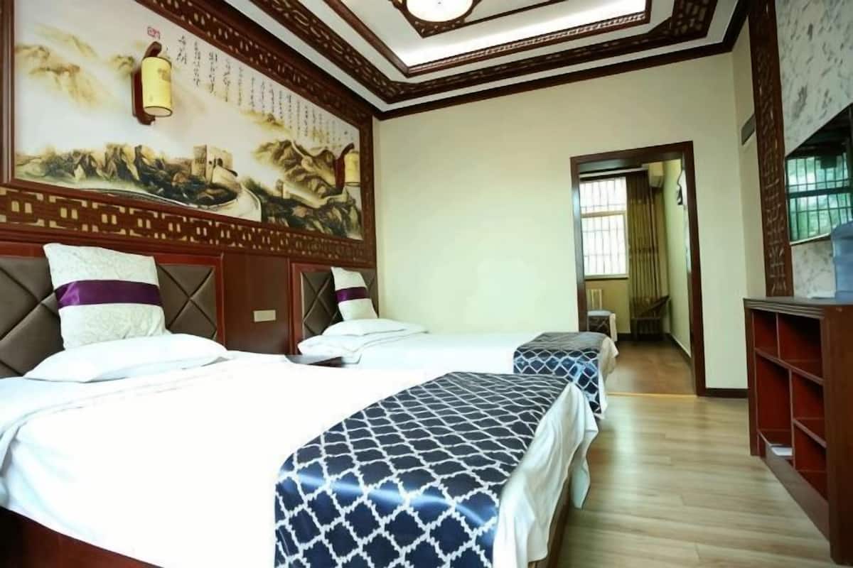 A hotel room with two beds, a traditional mural on the wall, and a wooden floor.