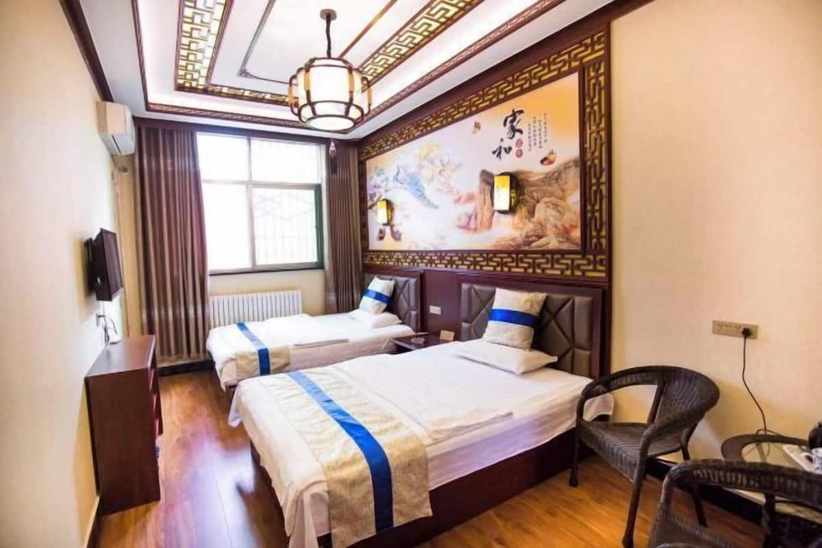 A hotel room with two beds, a wooden floor, a traditional wall mural, and a window with curtains.