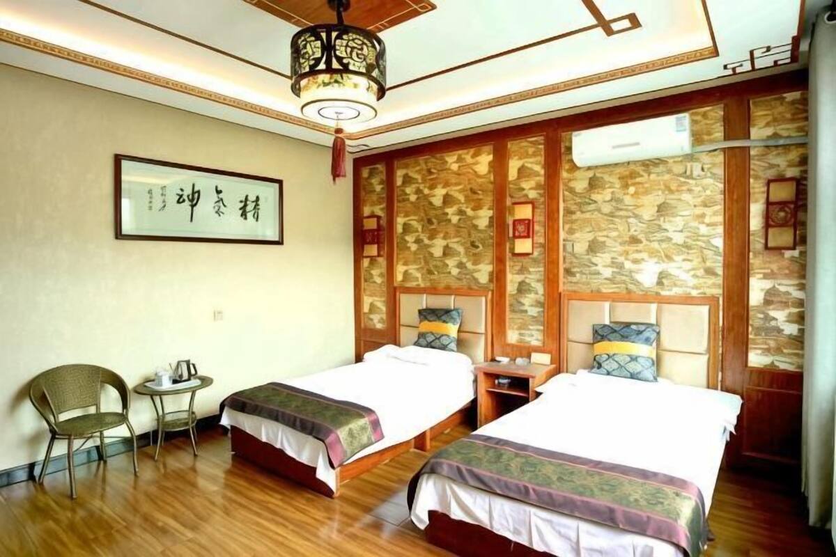 A hotel room with two beds, a small table, a chair, and a traditional wall decoration.
