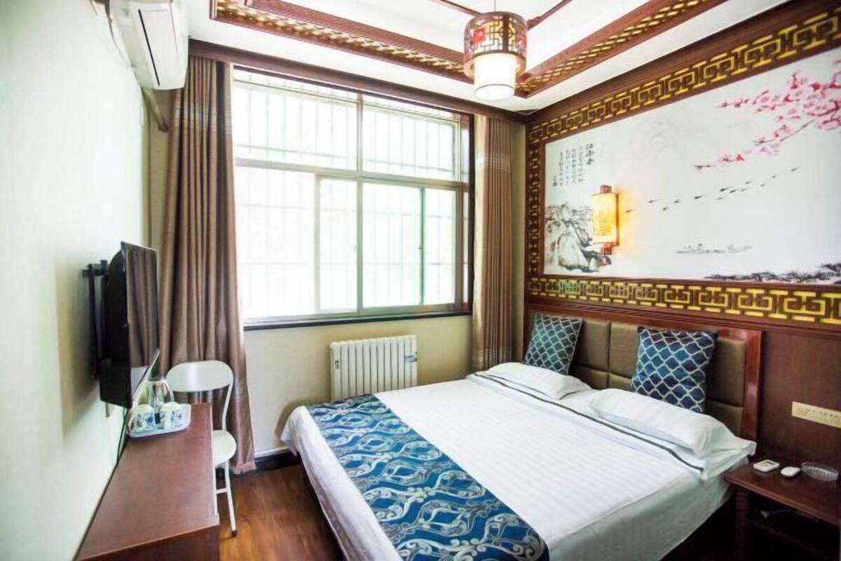 A hotel room with a bed, a desk, a chair, a television, and a large window.