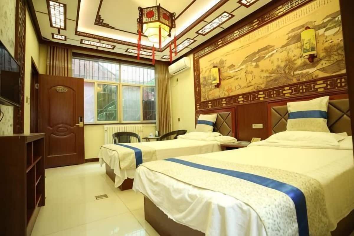 A hotel room with two beds, a desk, a chair, a radiator, and a window with curtains.