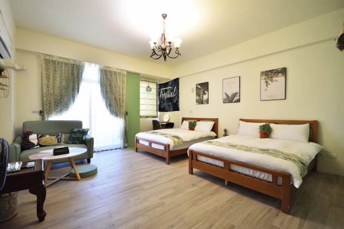 Una habitación con dos camas de madera, un sofá verde, una mesa de centro redonda y una araña.