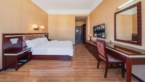 A hotel room with a bed, bedside table, desk, chair, and a large mirror.