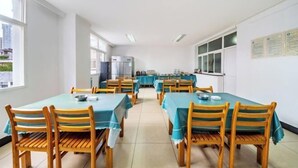 A dining area with tables covered in blue tablecloths and wooden chairs, large windows, and a view of buildings outside.