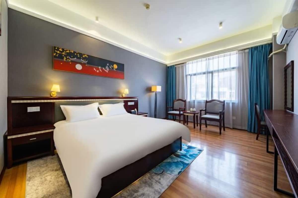 Habitación de hotel con una cama grande, un escritorio, una silla, una mesa y un cuadro en la pared.