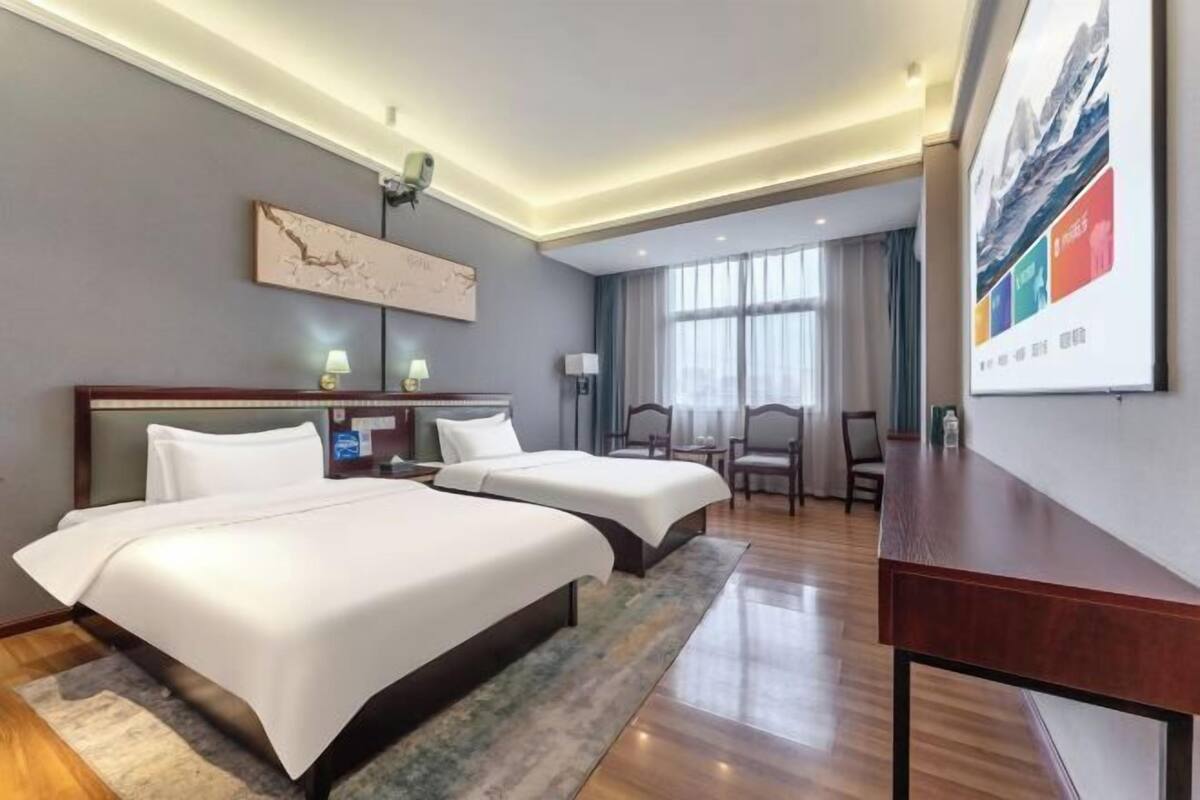 Una habitación de hotel con dos camas, un escritorio, una silla, una lámpara y un ventanal grande.