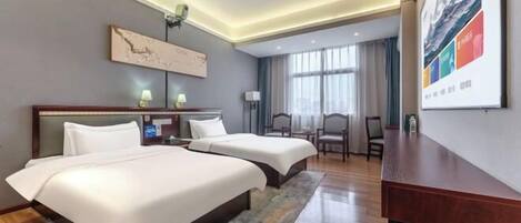 A hotel room with two beds, a desk, a chair, a lamp, and a large window.