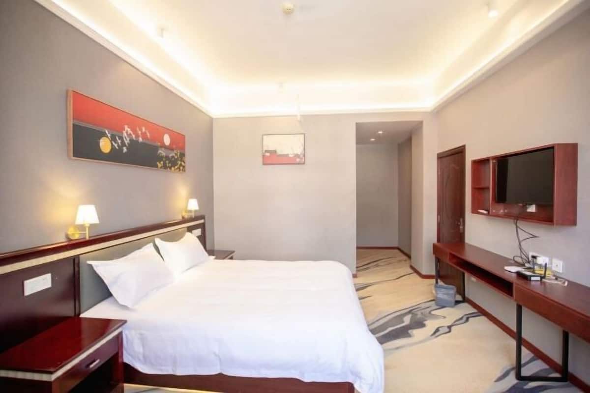 Habitación de hotel con cama, mesitas de noche, escritorio, televisor y obras de arte en las paredes.