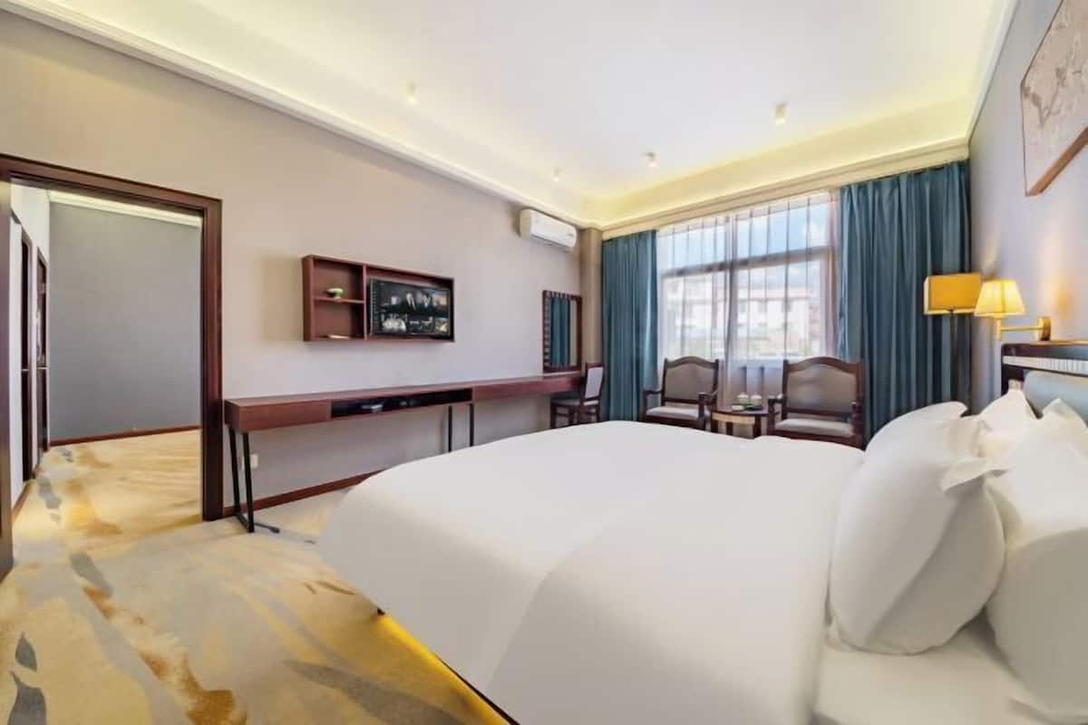 Habitación de hotel con una cama grande, escritorio, silla, televisor y ventana con cortinas.