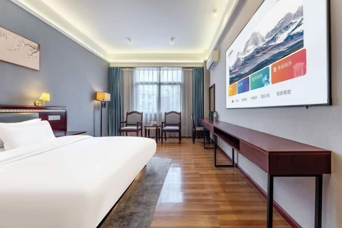 Habitación de hotel con cama, escritorio, silla, mesa y una pantalla grande en la pared.