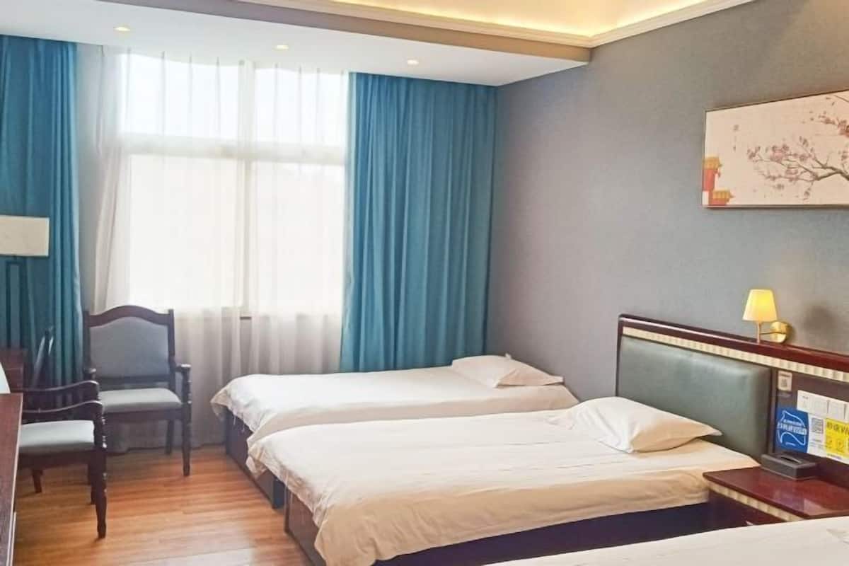 Habitación de hotel con dos camas, un escritorio, una silla y un ventanal con cortinas.