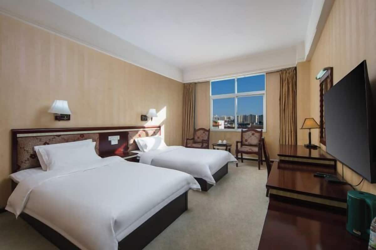 Habitación de hotel con dos camas, un escritorio, un televisor y ventana con vista a la ciudad.