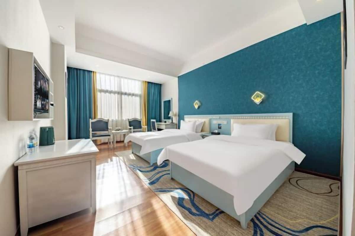Habitación de hotel con dos camas, un escritorio, una silla y un televisor.