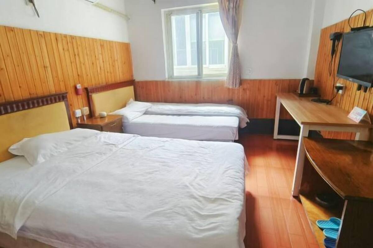 A hotel room with two beds, a wooden headboard, a television, and a window with curtains.