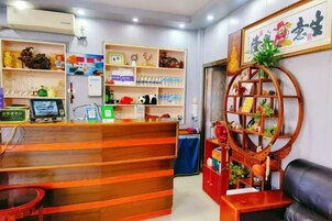 Un mostrador de recepción con una computadora, una silla azul y un estante de madera con diversos objetos.