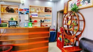 A reception area with a wooden reception desk, shelves with various items, a computer monitor, and a decorative wooden shelf with plants. - Qingshui Hostel (Shanghai)