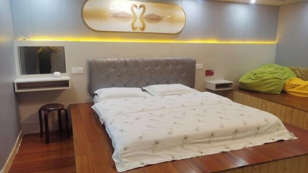 A modern bedroom with a large bed, a bedside table, a mirror, and a wall-mounted artwork. - Qingshui Hostel (Shanghai)