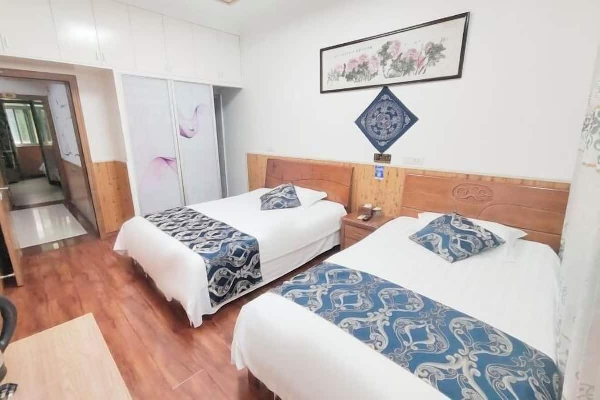 A hotel room with two beds, a wooden headboard, a nightstand, a framed picture, and a door leading to another room.