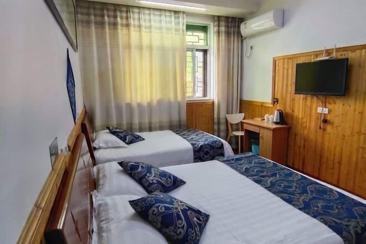 A hotel room with two beds, a wooden desk, a television, and a window with curtains.
