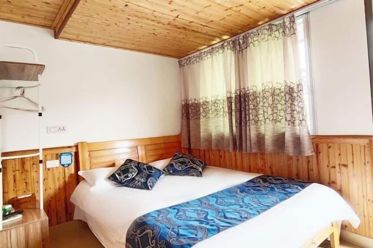 A wooden-paneled room with a bed, a bedside table, and a window with curtains.