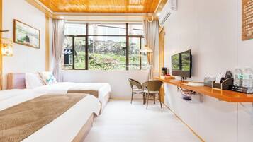 A hotel room with a wooden ceiling, a large window with a view of greenery, a desk with a chair, and a bed with a blanket.
