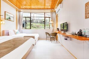 A hotel room with a wooden ceiling, a large window with a view of greenery, a desk with a chair, and a bed with a blanket. - Queen's Mountain Oxygen Heart Valley Mountain Resort (Lianshan)