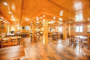 A spacious indoor area with wooden flooring and tables, featuring a central open space and multiple seating areas. - Queen's Mountain Oxygen Heart Valley Mountain Resort (Lianshan)