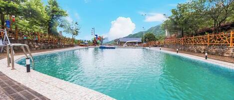 A swimming pool with a clear blue water, surrounded by a stone deck and a metal fence.