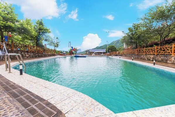 A swimming pool with a clear blue water, surrounded by a stone deck and a metal fence. - Queen's Mountain Oxygen Heart Valley Mountain Resort (Lianshan)
