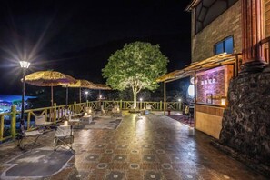 Ein Außenbereich mit Terrasse, Tischen, Stühlen, einem Baum und einem Gebäude mit Steinverkleidung.