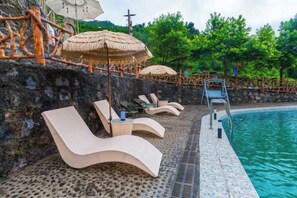 A poolside area with lounge chairs, umbrellas, and a stone wall. - Queen's Mountain Oxygen Heart Valley Mountain Resort (Lianshan)