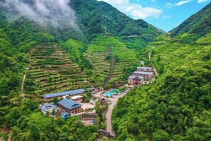 Terraced tea plantations with buildings at the base, surrounded by lush greenery and mountains. - Queen's Mountain Oxygen Heart Valley Mountain Resort (Lianshan)