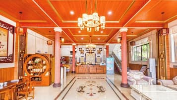 A hotel lobby with a wooden ceiling, a central chandelier, a reception desk, and a patterned floor.