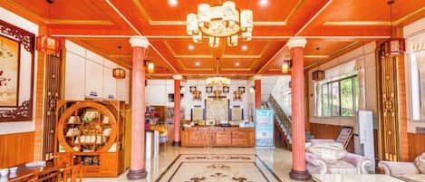 A hotel lobby with a wooden ceiling, a central chandelier, a reception desk, and a patterned floor.