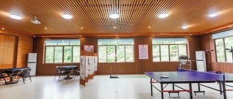 A room with a ping pong table, wooden ceiling, and large windows.