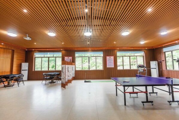 Ein Zimmer mit einem Tischtennis-Tisch, Holzboden und großen Fenstern.